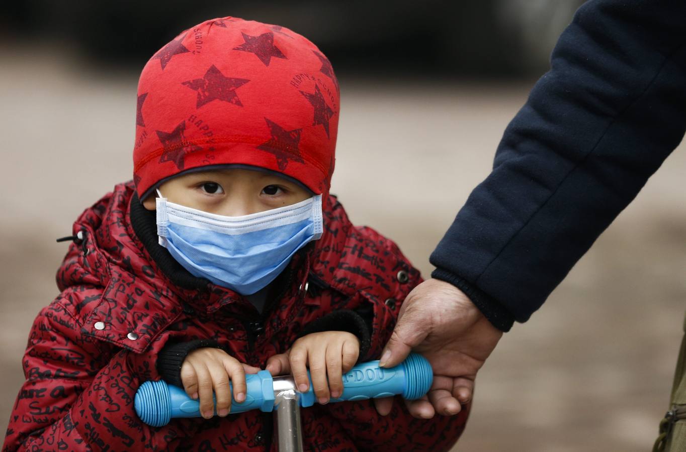 Un niño monta en triciclo protegido con una mascarilla, en Pekín (China)