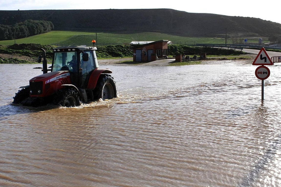 Un tractor circula por una carretera de acceso a Benegiles, anegada tras el desbordamiento del río Valderaduey. 