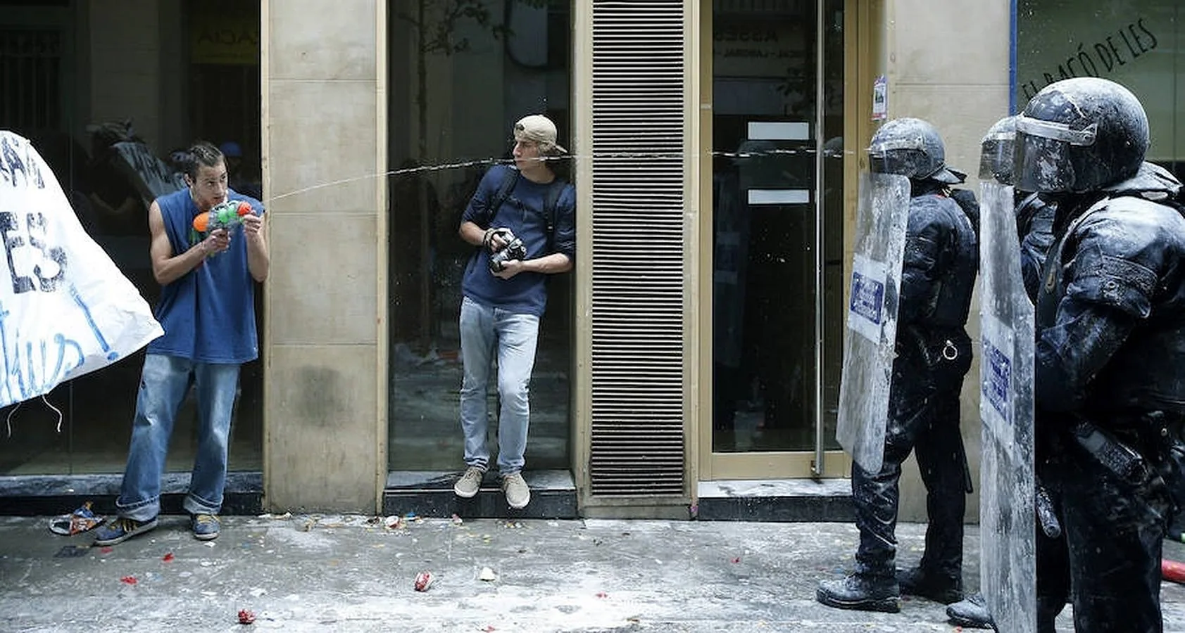 Un manifestante lanza agua a los antidisturbios en el barrio de Gràcia, donde unas doscientas personas se han concentrado en los alrededores del "banco okupado"