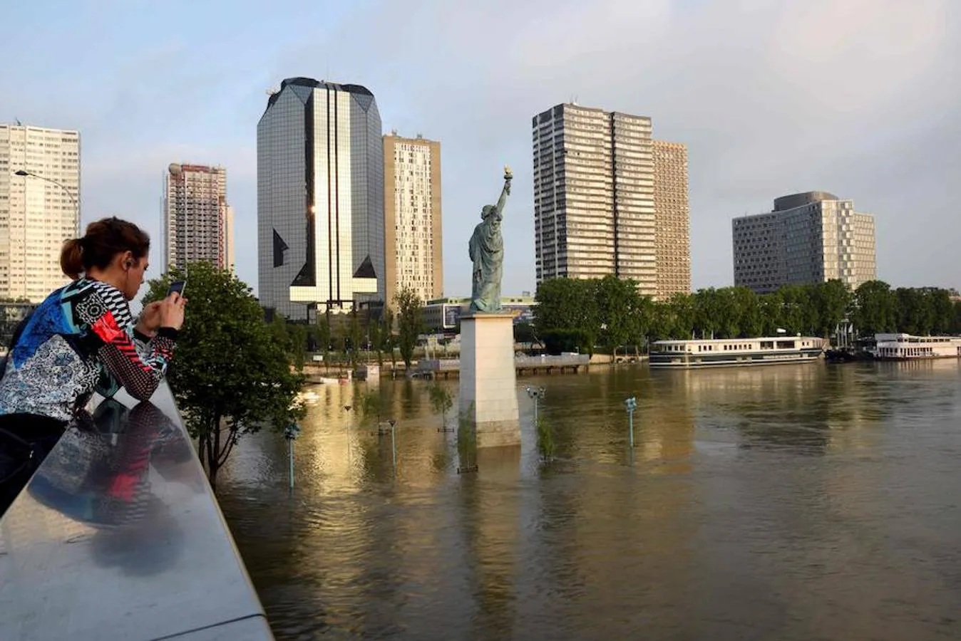 Una muchacha mira el móvil en un puente ubicado en frente de una réplica de la Estatua de la Libertad en el río Sena 