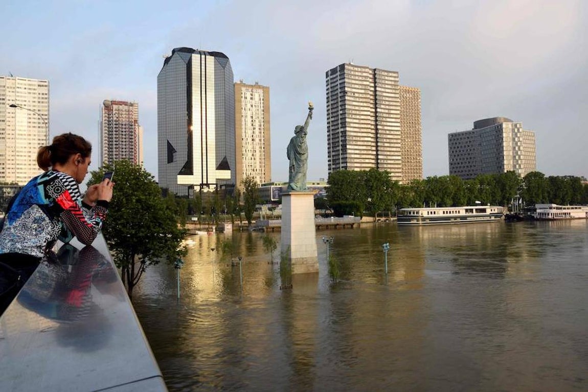 Una muchacha mira el móvil en un puente ubicado en frente de una réplica de la Estatua de la Libertad en el río Sena. 