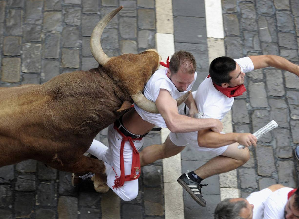 El toro colorado ha tomado la cabeza y ha llegado a la plaza del Ayuntamiento barriendo el vallado derecho, donde varios corredores han caído al suelo y uno de ellos ha sido enganchado por las astas y volteado