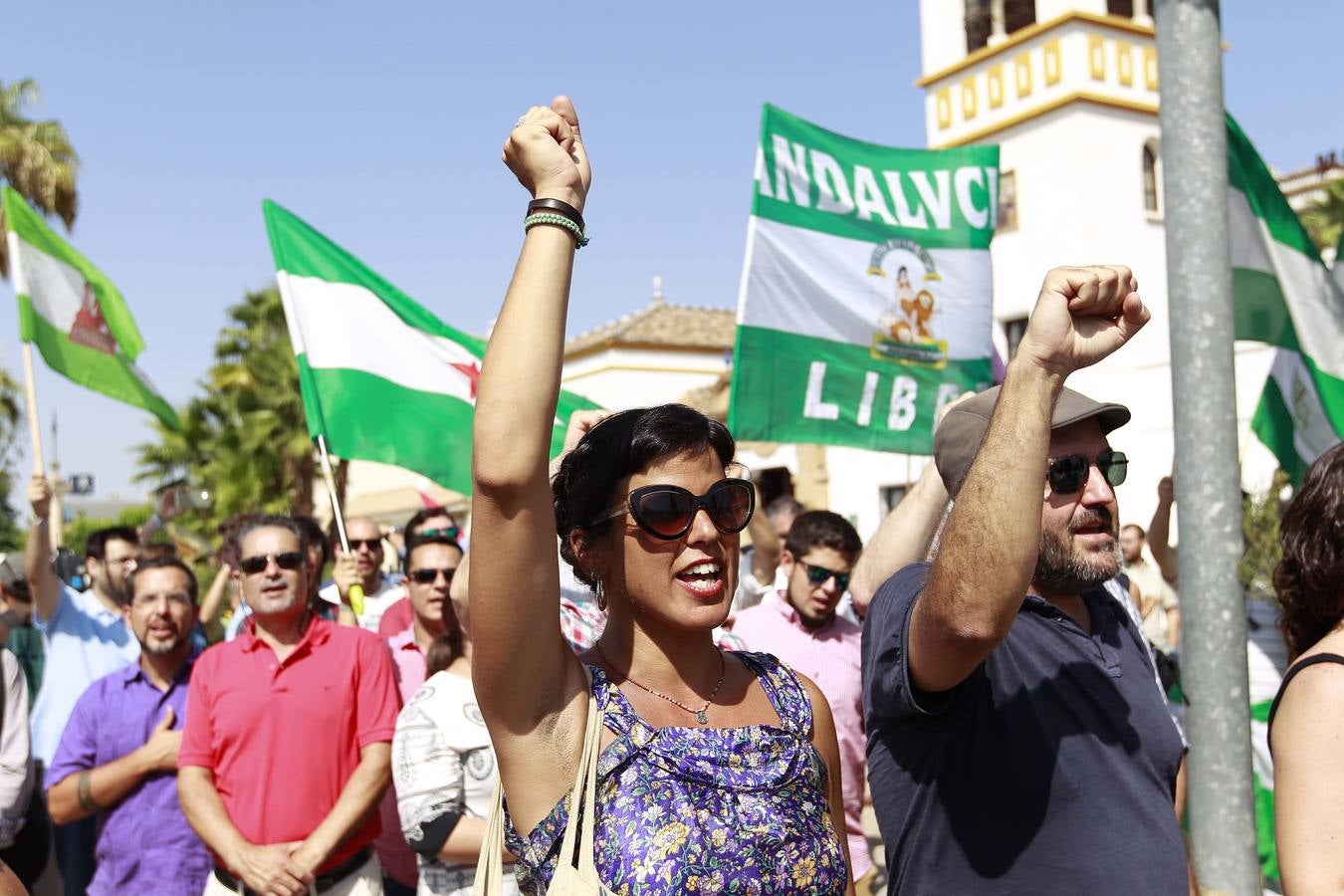 Teresa Rodríguez, de Podemos, cantando el himno andaluz con el puño en alto.. Al fondo, su compañero Sergio Pascual con la mano sobre el pecho