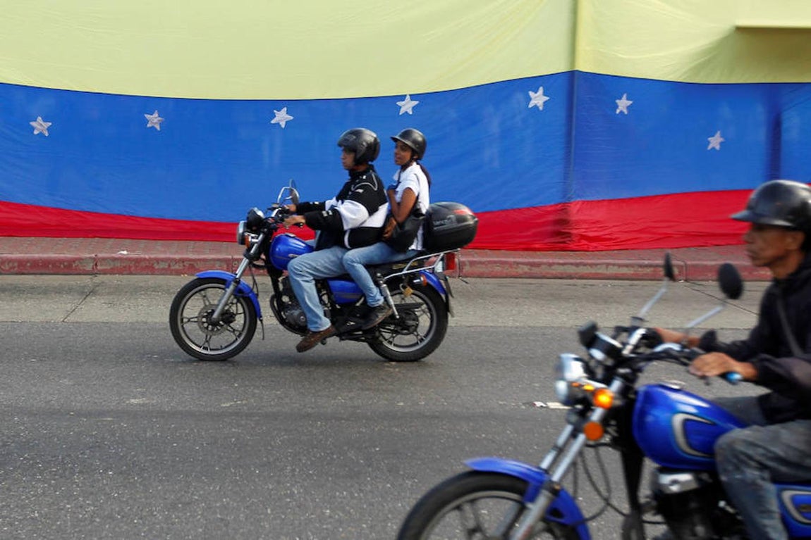Gente en motocicleta pasa junto a una bandera venezolana en Caracas. 