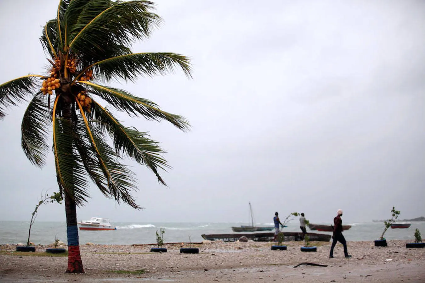 Haitianos residentes en Les Cayes caminan junto a sus botes antes de la llegada del huracán a su país