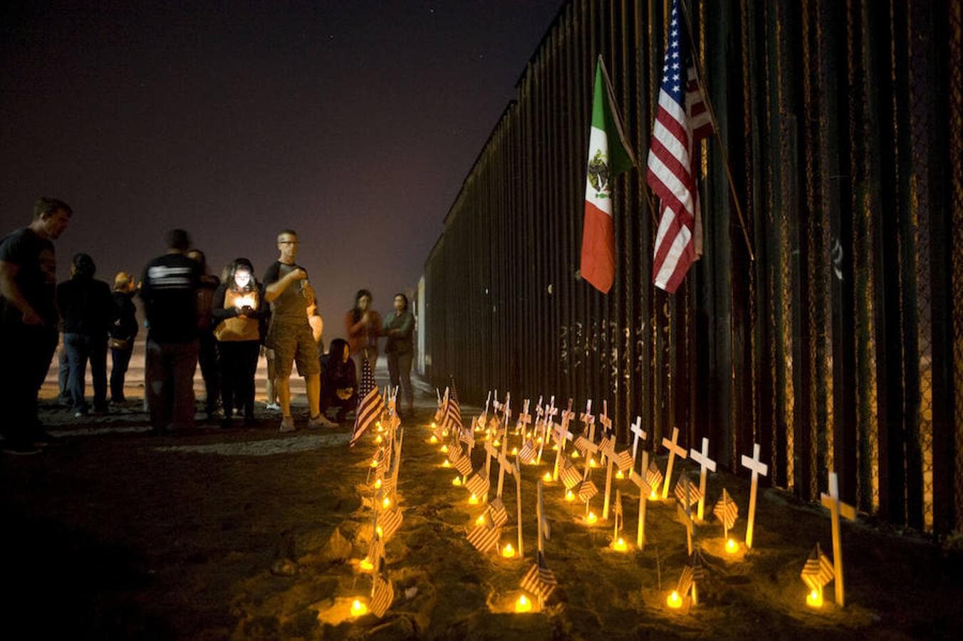 Personas asisten a una vigilia junto reja que divide la frontera de los EEUU con México en honor a los veteranos deportados, durante la conmemoración del día del veterano en Tijuana, México