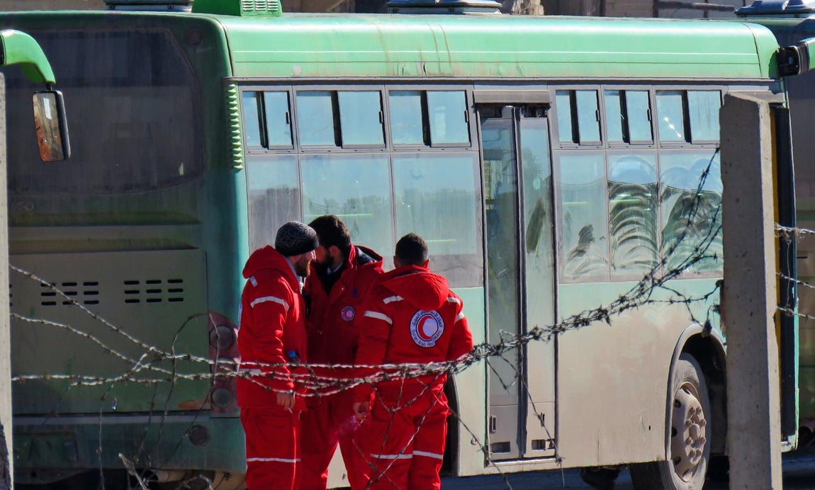 Un grupo de miembros de la Media Luna Roja espera junto a los autobuses preparados para evacuar a los rebeles sirios y sus familias de Alepo. 