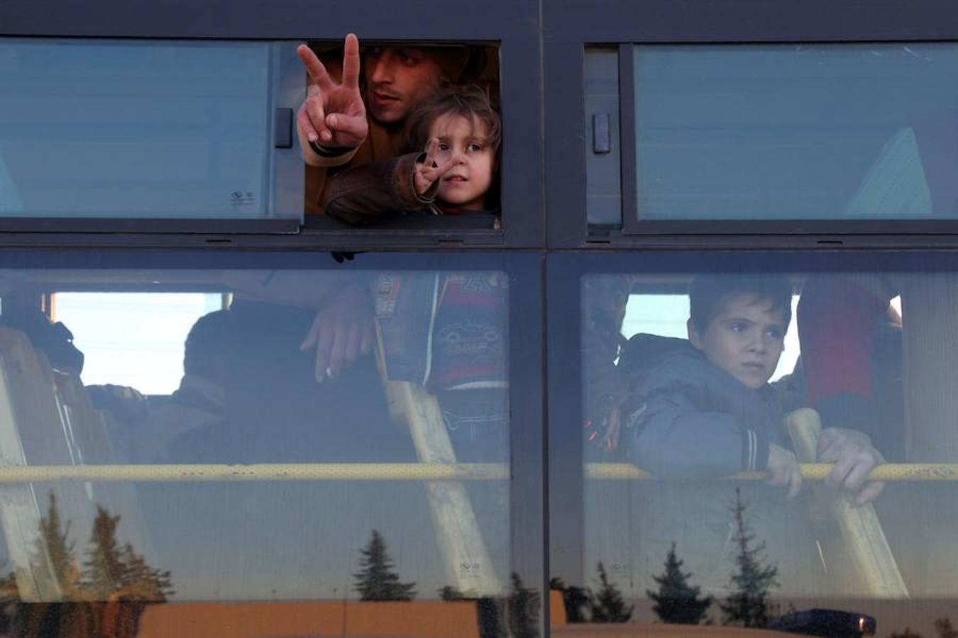 Un hombre y una niña sirios son evacuados en un autobús de la zona rebelde del este de Alepo mientras hacen el signo de la victoria con la mano.