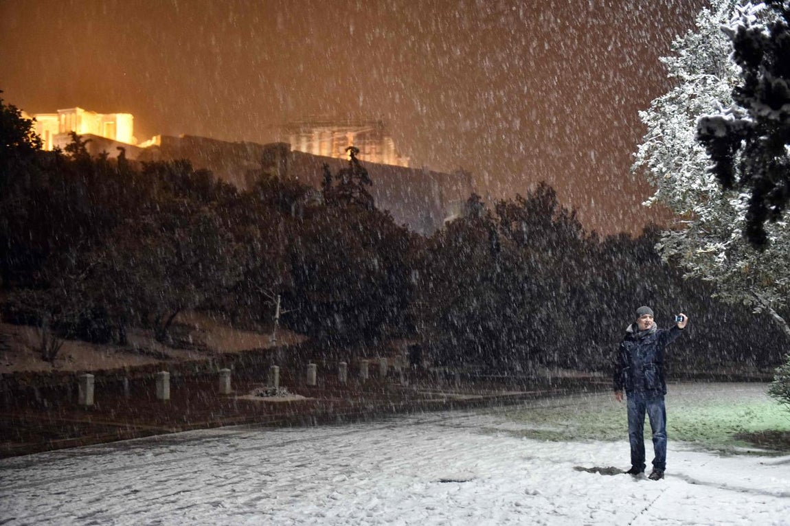 Un hombre se hace una foto con el Partenón de Atenas, cubierto por la nieve, de fondo. 