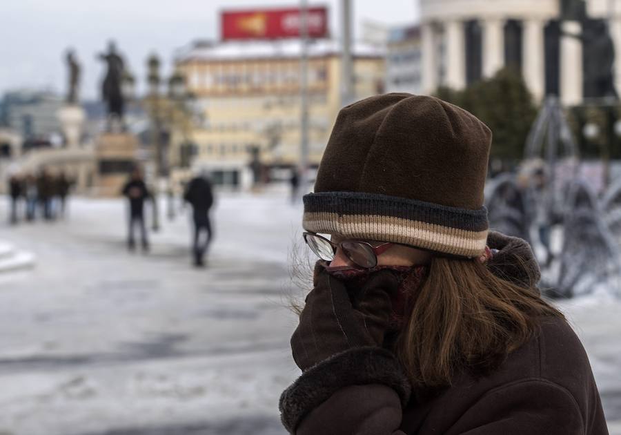 Una mujer se cubre la cara mientras camina por la plaza principal cubierta de nieve y hielo en Skopje, Macedonia