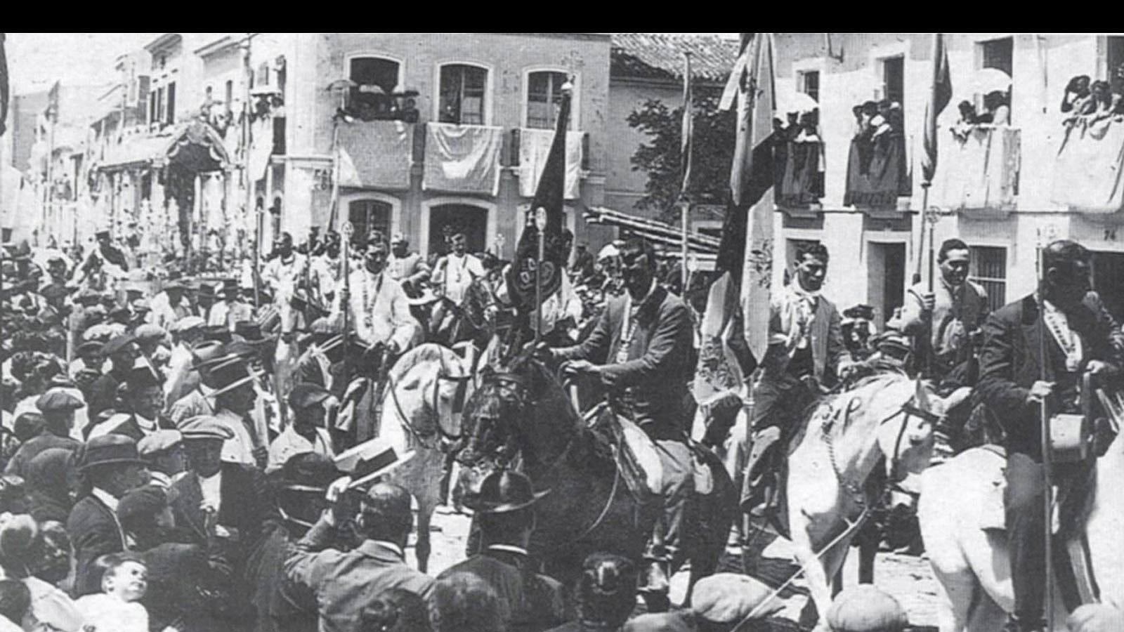 Año 1917. Salida de la Hermandad del Rocío de Triana de la iglesia parroquial de San Jacinto. En ella se puede reconocer a Carlos Astolfi Roldán, quien, pañuelo al cuello, porta a caballo la bandera de la hermandad. Se puede apreciar todo lo que ha cambiado la esquina de la calle San Jacinto con Pagés del Corro. A la derecha se ve la casa donde hoy está la oficina de Correos..