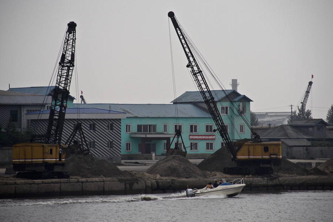 Una lancha de turistas chinos pasa junto al muelle industrial de Sinuiju, donde dos grúas cargan arena. 