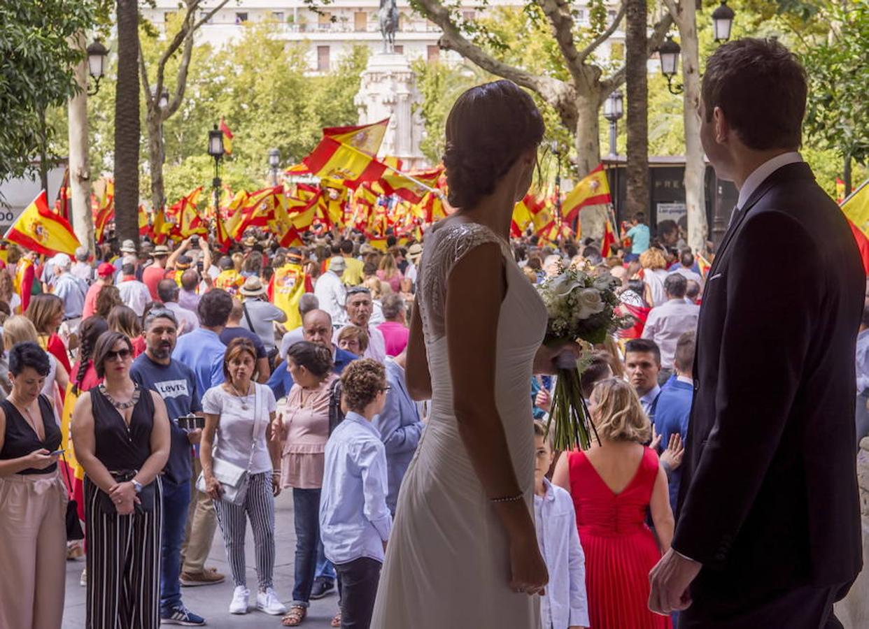 Una pareja de recién casados observa desde la puerta del Ayuntamiento de Sevilla a las miles de personas que han salido hoy a la calle en Sevilla con banderas españolas en demanda de la unidad de la nación y contra el referéndum catalán, en una manifestación que se ha desarrollado sin incidentes.. 