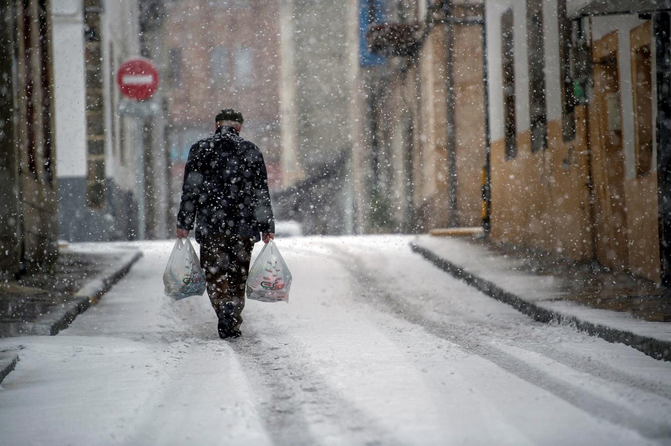 Reinosa (Cantabria). Un hombre camina por la calle en la localidad cántabra de Reinosa, donde la nieve obliga a usar cadenas en la A-67 e impide el paso a camiones por el puerto de Pozazal,