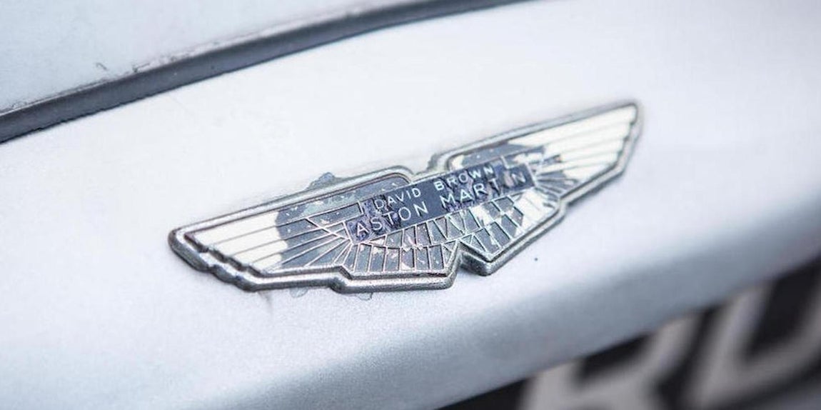 Aston Martin DB5. Su forma era mucho más alargada. Uno de sus distintivos, los faros con capucha. Su elegancia y estética deportiva lo llevaron a la gran pantalla. Fue el primer Aston Martin que condujo el Agente 007, lo hizo en la película «Goldenfinger» en 1965, era de color plata con interiores en rojo y estaba equipado con un lanzacohetes