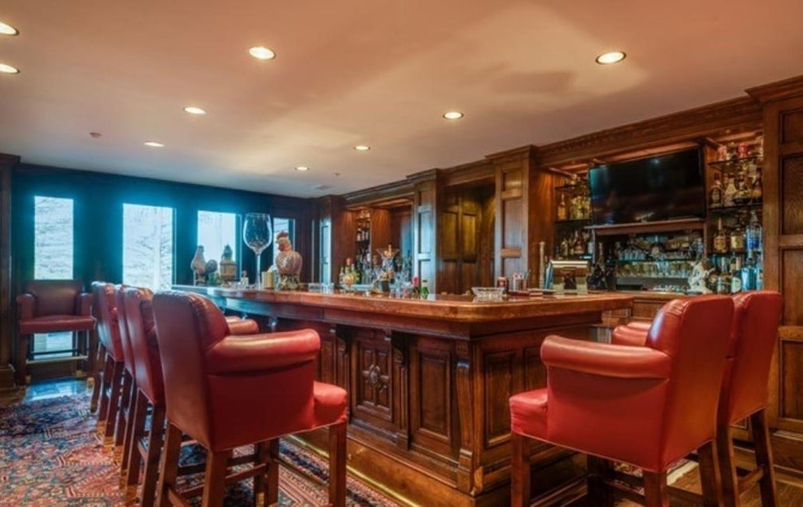 Bar. Entre las estancias más lujosas encontamos una barra de bar dotada con siete taburetes de madera y cuero que, en la imágen, reposan sobre una alfombra persa. No es el rincón más llamativo de la mansión, también tiene gimnasio, peluqueria y un spa para desconectar del ajetreo del día a día. Uno de los lugares más extravagantes de la finca es un refugio antiaéreo