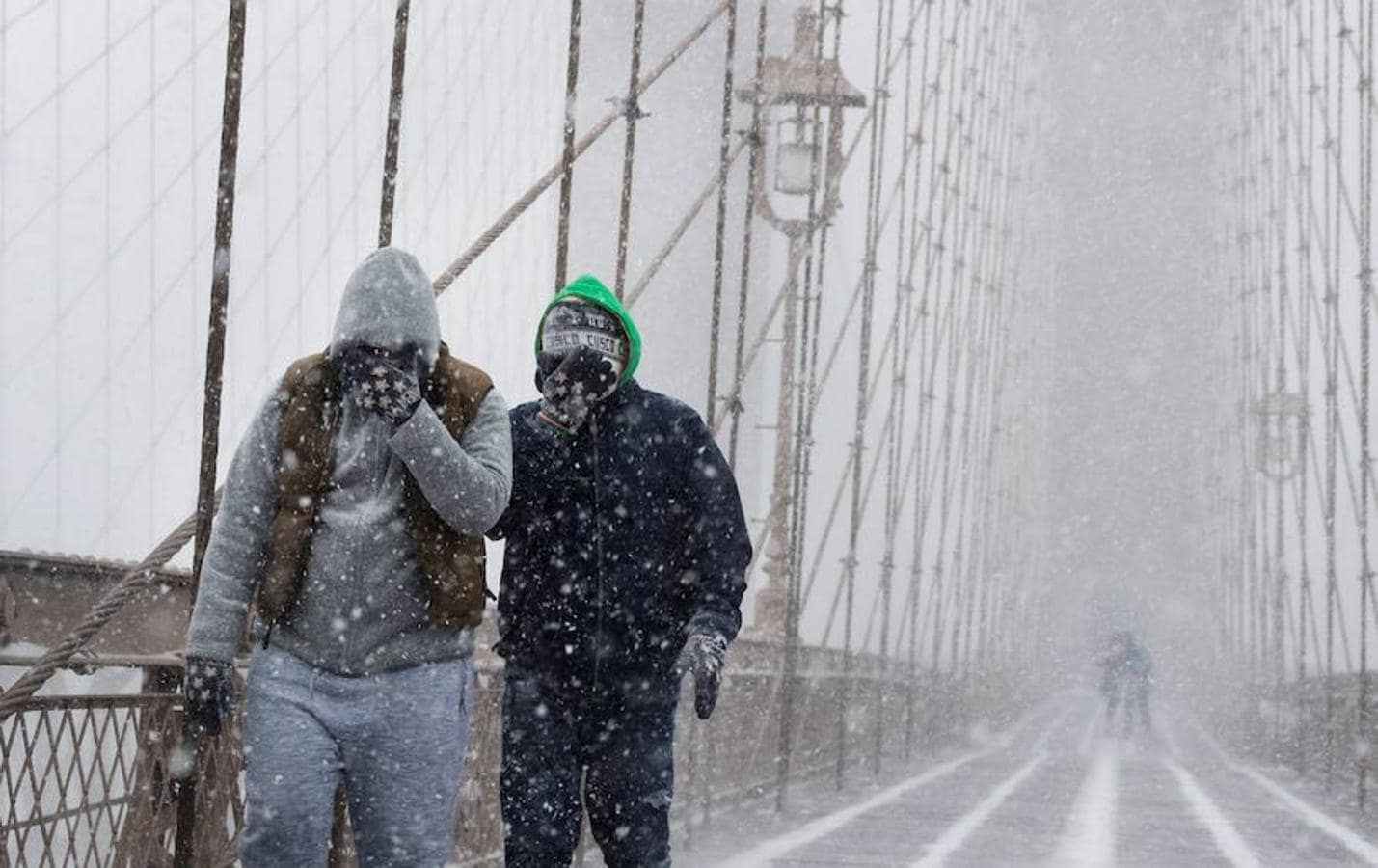 Peatones se protegen de la nieve y del viento mientras cruzan el puente de Brooklyn durante una tormenta de viento y nieve, en Nueva York.. 
