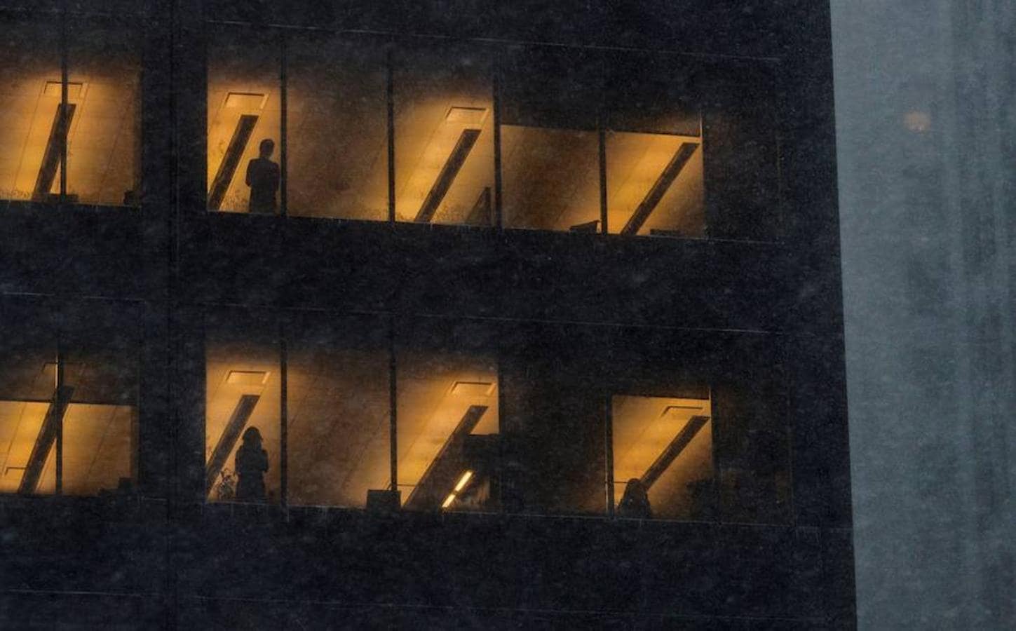 Varias personas se asoman a las ventanas de un edificio de oficinas durante la tormenta de viento y nieve de Nueva York.. 