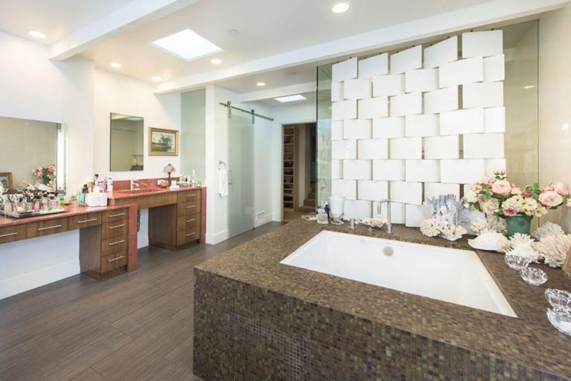 Baño con libros. En los cuartos de baño destaca una estantería con libros, una claraboya en el techo y suelo radiante de porcelanato que imita el estilo de la madera