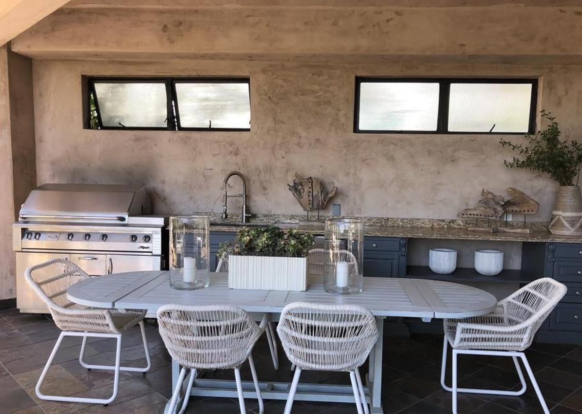 Estilo mediterráneo contemporáneo. La casa es de estilo mediterraneo contemporáneo, se caracteriza por incluir elementos como arcos, suelos de terrazo, tejados de teja y una distribución en estancias muy amplias de techos altos. La imagen muestra la cocina exterior, de estilo rústico, perfecta para las veladas al aire libre