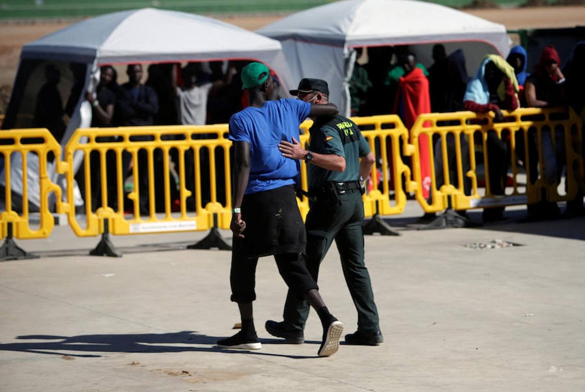 Un inmigrante rodea con el brazo a un guardia civil que cuida y vigila a las personas que llegan en patera a las costas de Cádiz y son trasladadas al pabellón «Antonio Gavira», en el municipio Los Barrios, cerca de Algeciras.. 