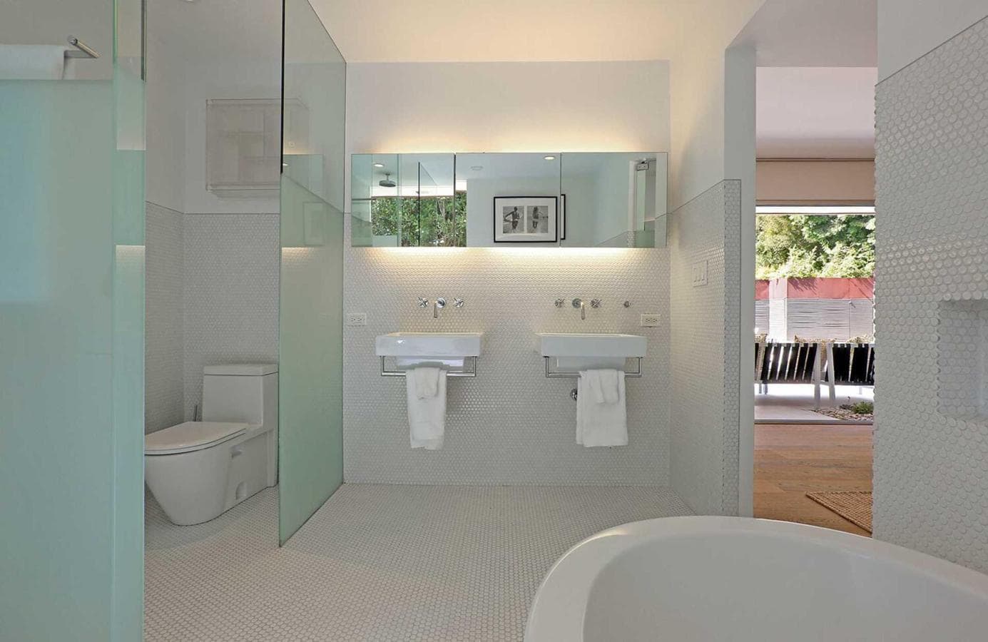 Cuarto de baño. Está revestido en pulcro azulejo blanco y los espacios están separados con cristal translúcido. Su diseño sigue la línea del resto de la vivienda, es moderno y minimalista