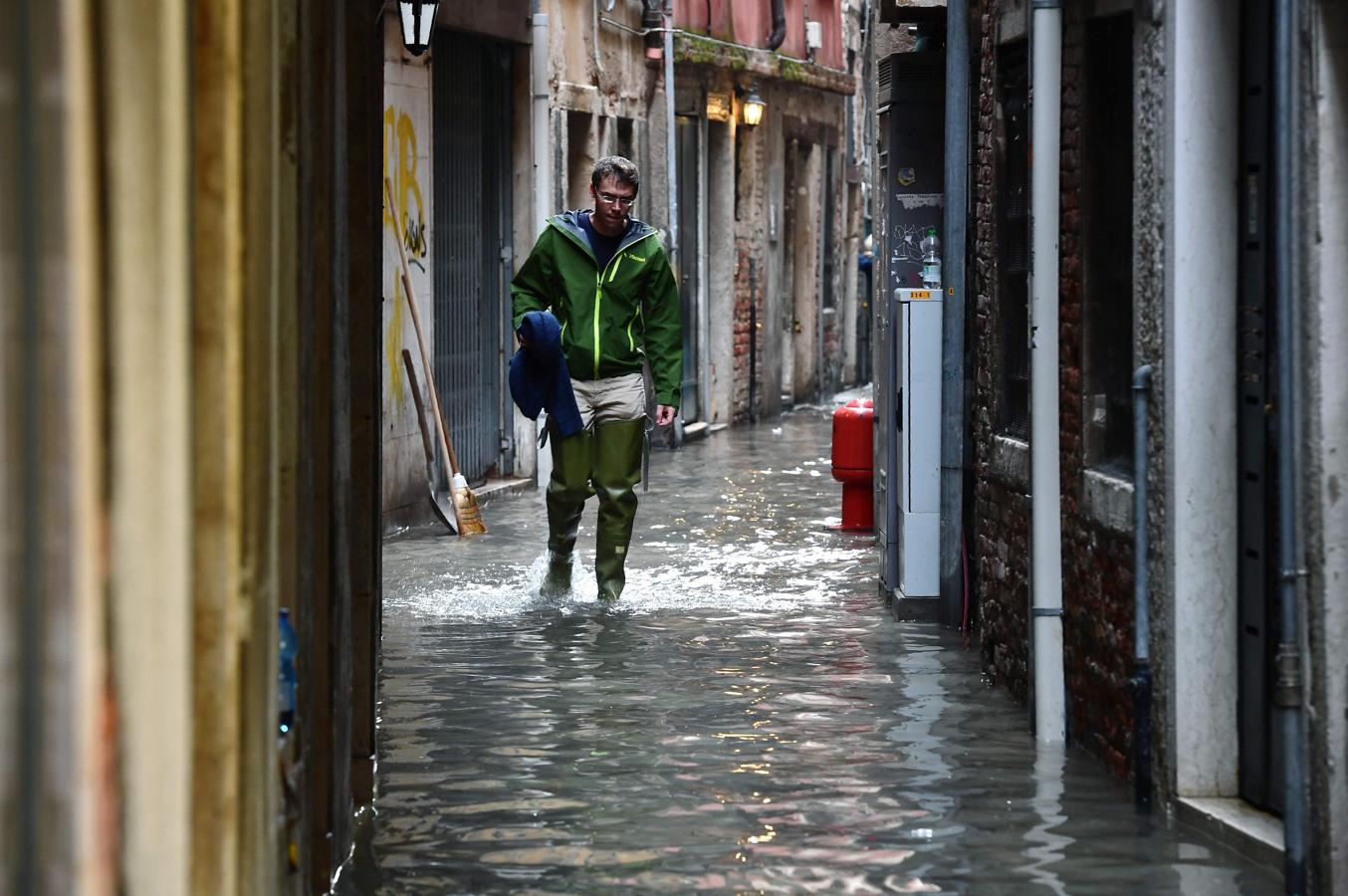 Un hombre, pertrechado con botas largas de agua, camina por una estrecha calle del casco histórico veneciano que está totalmente anegada de agua.. 