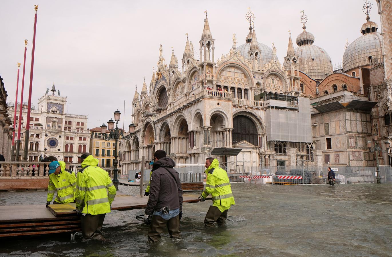 Un grupo de trabajadores construye un puente con unos tablones para tener un lugar donde poder caminar sobre tierra firme en Venecia.. 