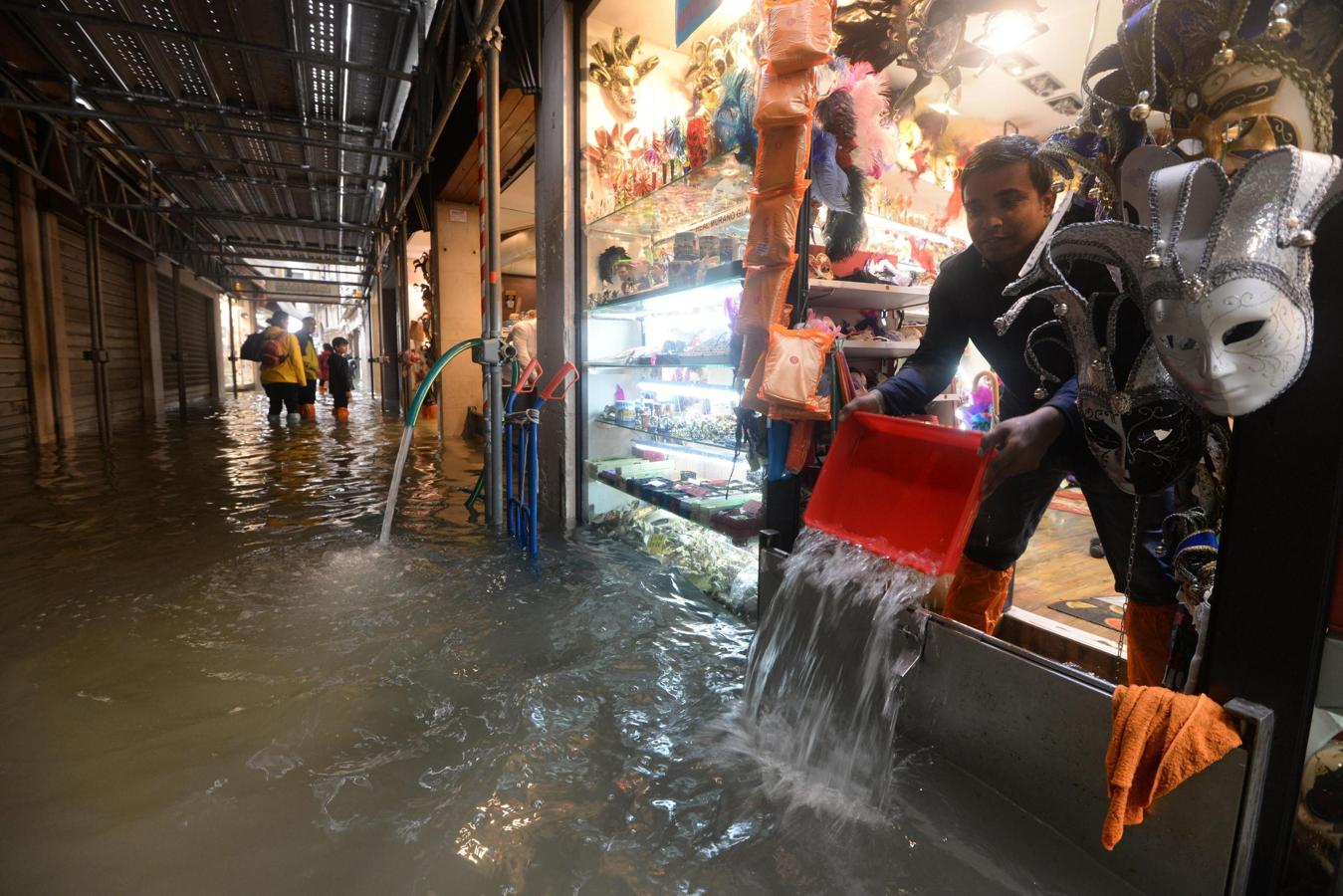 Un tendero, que se vio sorprendido por las lluvias, achica agua de su tienda en Venecia.. 