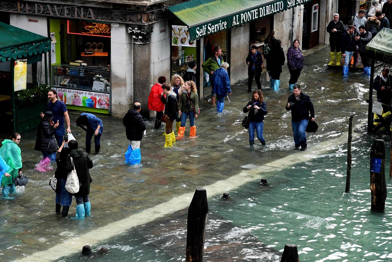 Varias de personas atraviesan la calle, que yace inundada, cerca del Puente de Rialto (Venecia).. 