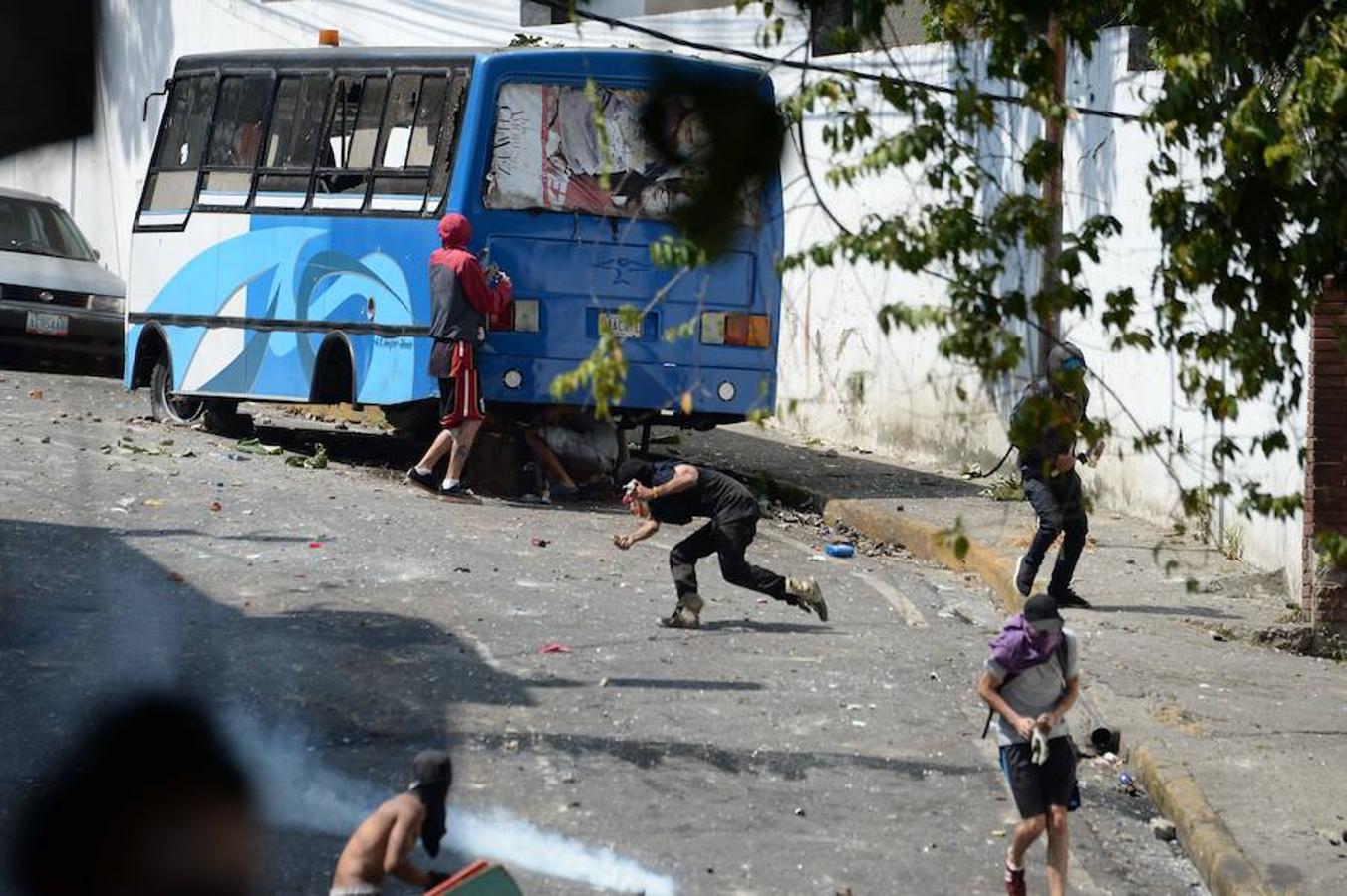 Las imágenes más dramáticas de la sublevación militar en Venezuela. Un grupo de manifestantes lanza objetos a las fuerzas de seguridad bolivarianas y se protege tras un autobús en parte calcinado