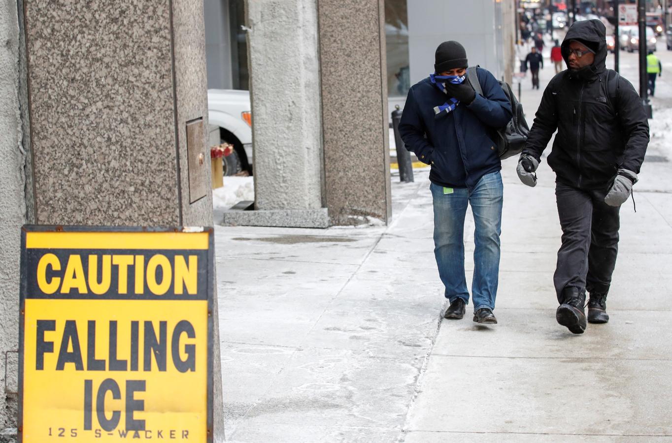 Dos hombres caminan durante la ola de frío polar en Chicago ante un cartel que avisa del peligro de caída por hielo.. 