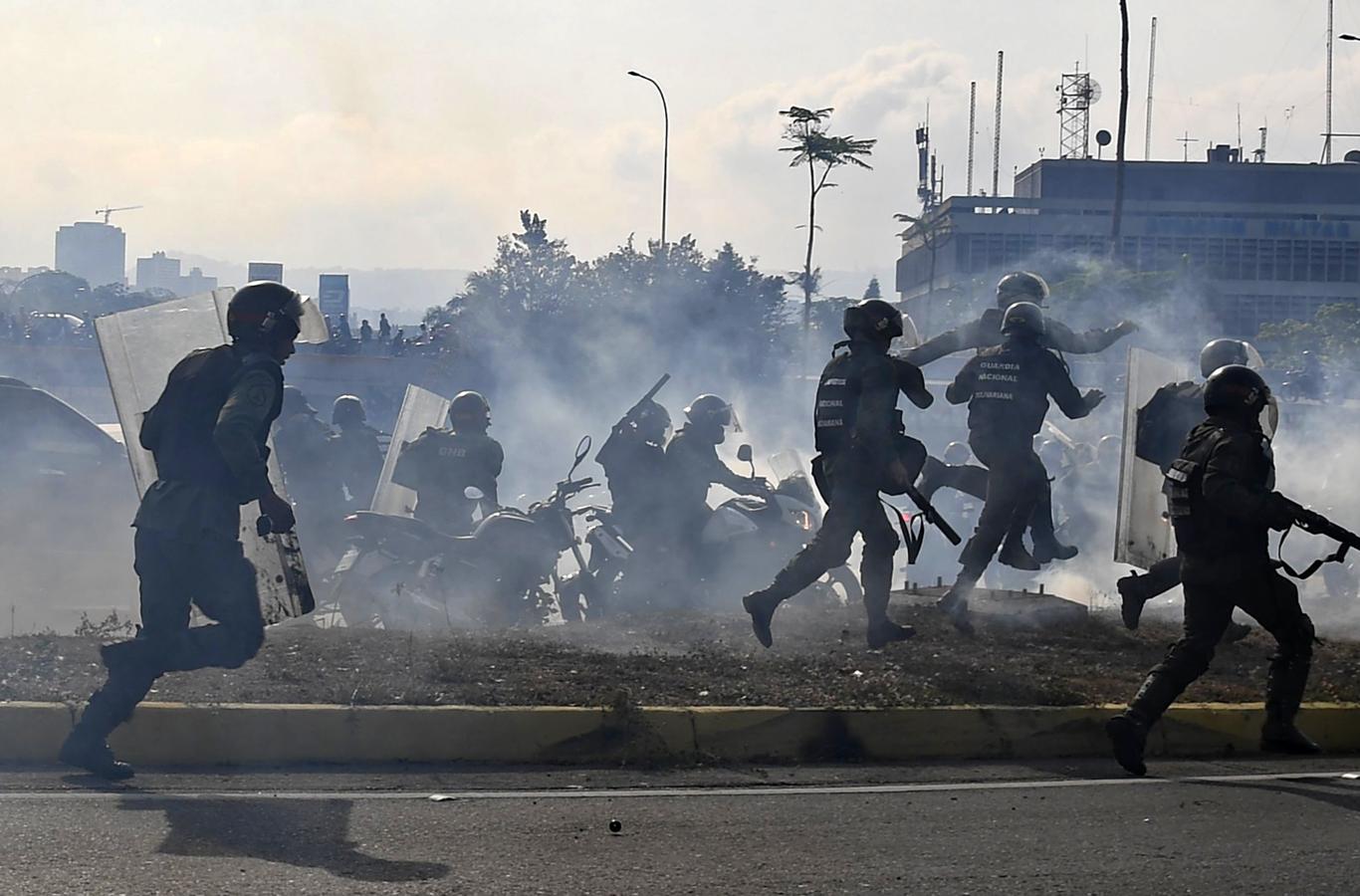 Miembros de la Guardia Nacional Bolivariana leales a Maduro corren bajo una nube de gas lacrimógeno. 