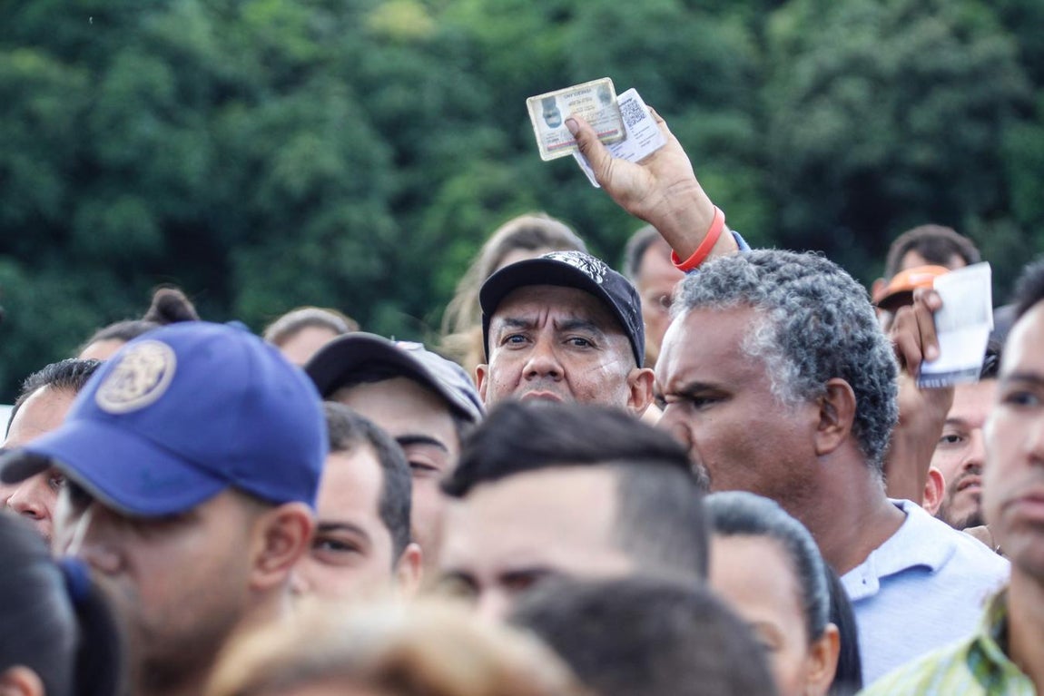 Un hombre eleva su documento de identificación en medio del paso de la frontera. 