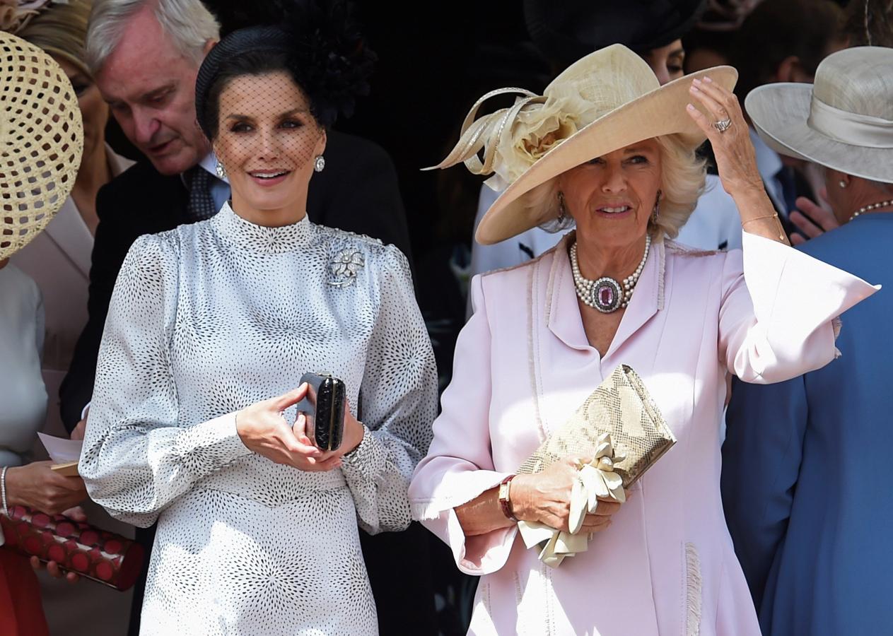 Doña Letizia luce un recatado vestido blanco con pequeñas motas oscuras de la marca sevillana Cherubina y un tocado gris marengo con una flor lateral y plumas de oca. 