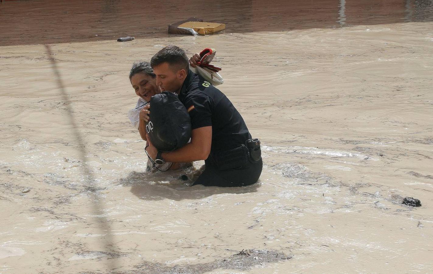 Un guardia civil ayuda a una vecina de Almoradí este viernes tras la rotura del muro del cauce del río Segura por la crecida del río que ha provocado el desbordamiento a la entrada de la población. 