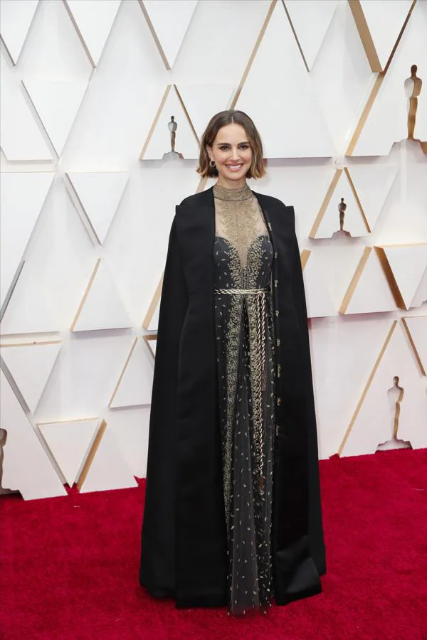 Natalie Portam ha sido una de las ganadoras de la alfombra roja de los Oscar con este vestido negro de Dior con escote en «V» y bordados dorados al que le ha sumado una capa bordada. 
