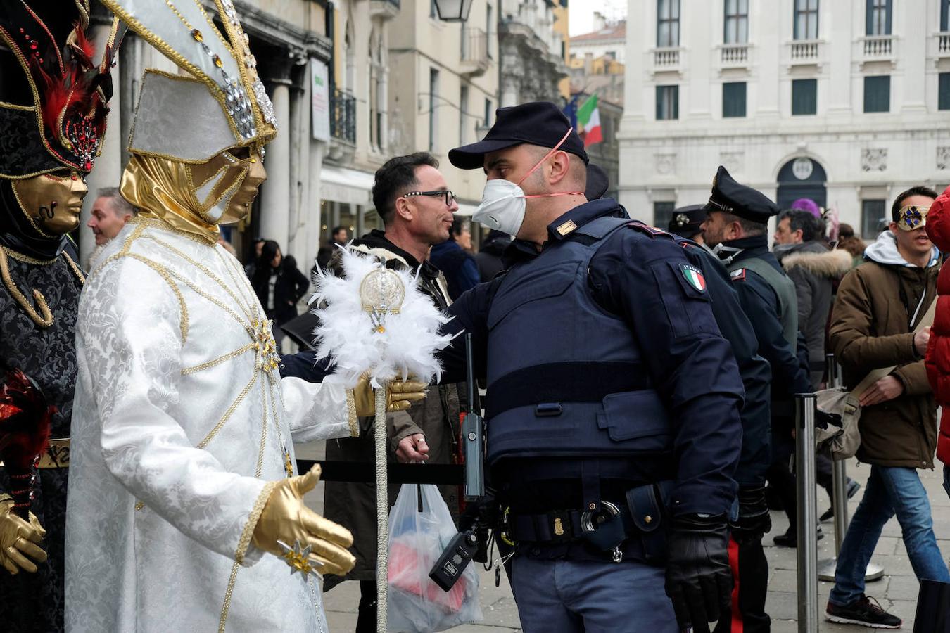 Un guardia con una mascarilla registra a una persona disfrazada en Venecia. 