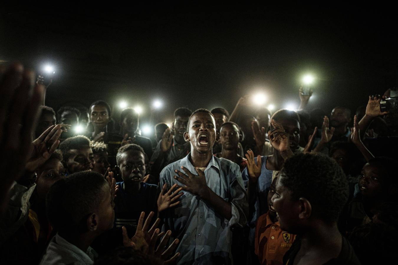 La ganadora, el grito pacífico de Sudán. El fotógrafo japonés Yasuyoshi Chiba ha sido galardonado este jueves con el World Press Photo por su fotografía del grito pacífico de un grupo de jóvenes en Sudán, que iluminaban con sus teléfonos móviles a un chico mientras recitaba un poema a la multitud en medio de un apagón durante las protestas en Jartum el año pasado. La instantánea se titula «Straight Voice» (Voz erguida)