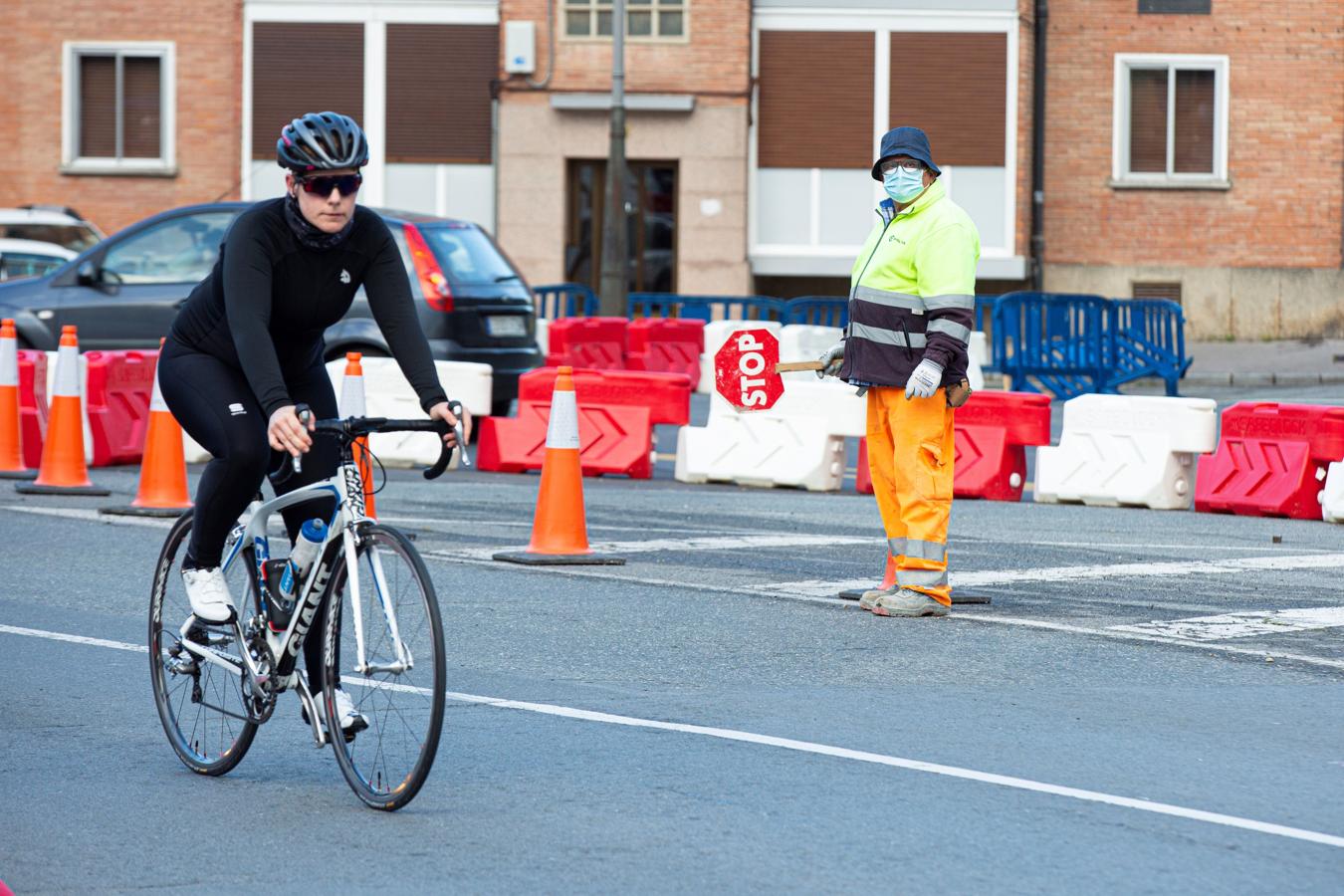 Que no falte el pedaleo. Una mujer pasea en bicicleta en una calle de Vitoria, mientras el trabajador de una obra pública la observa, con una señal para interrumpir el tráfico en la mano