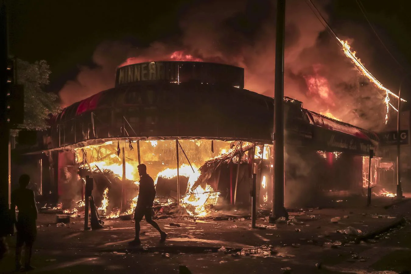 Disturbios en Mineápolis. Un hombre camina entre las llamas, cerca de una tienda de licores incendiada y próxima a una comisaría de Mineápolis