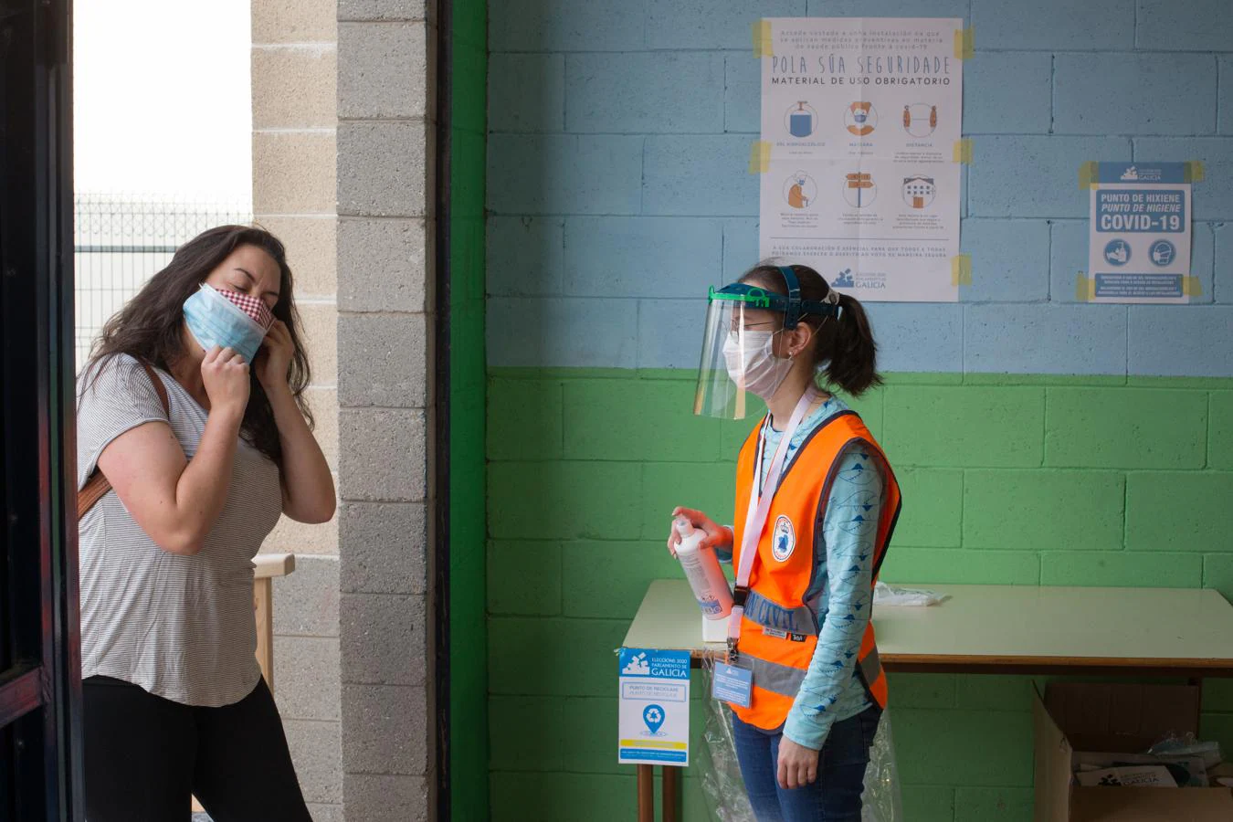 La jornada ha estado marcada por estrictas medidas de seguridad para evitar aglomeraciones y contagios en los colegios. En la imagen, una empleada de Protección Civil se dispone a echar gel desinfectante en las manos de una electora en Burela (Lugo).. 