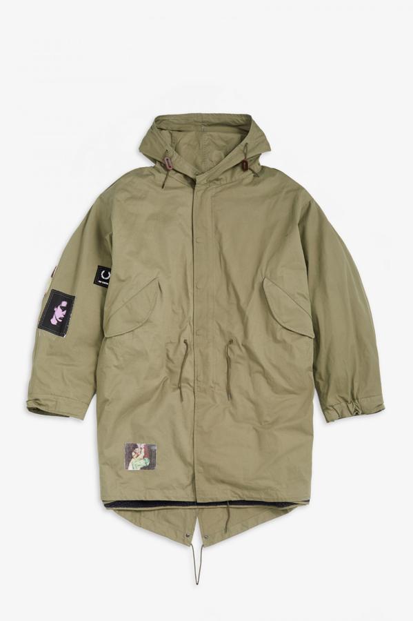 Parka con forro extraíble, de Raf Simons para Fred Perry. Modelo de corte oversize con capucha y bajo asimétrico en algodón verde oliva con forro de felpa de algodón y parches serigrafiados en cuerpo, espalda y mangas. Precio: 780€.