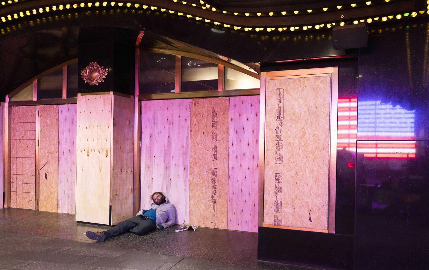 Un sin techo, ajeno a todo, duerme apoyado en un edificio tapiado frente a Time Square. 