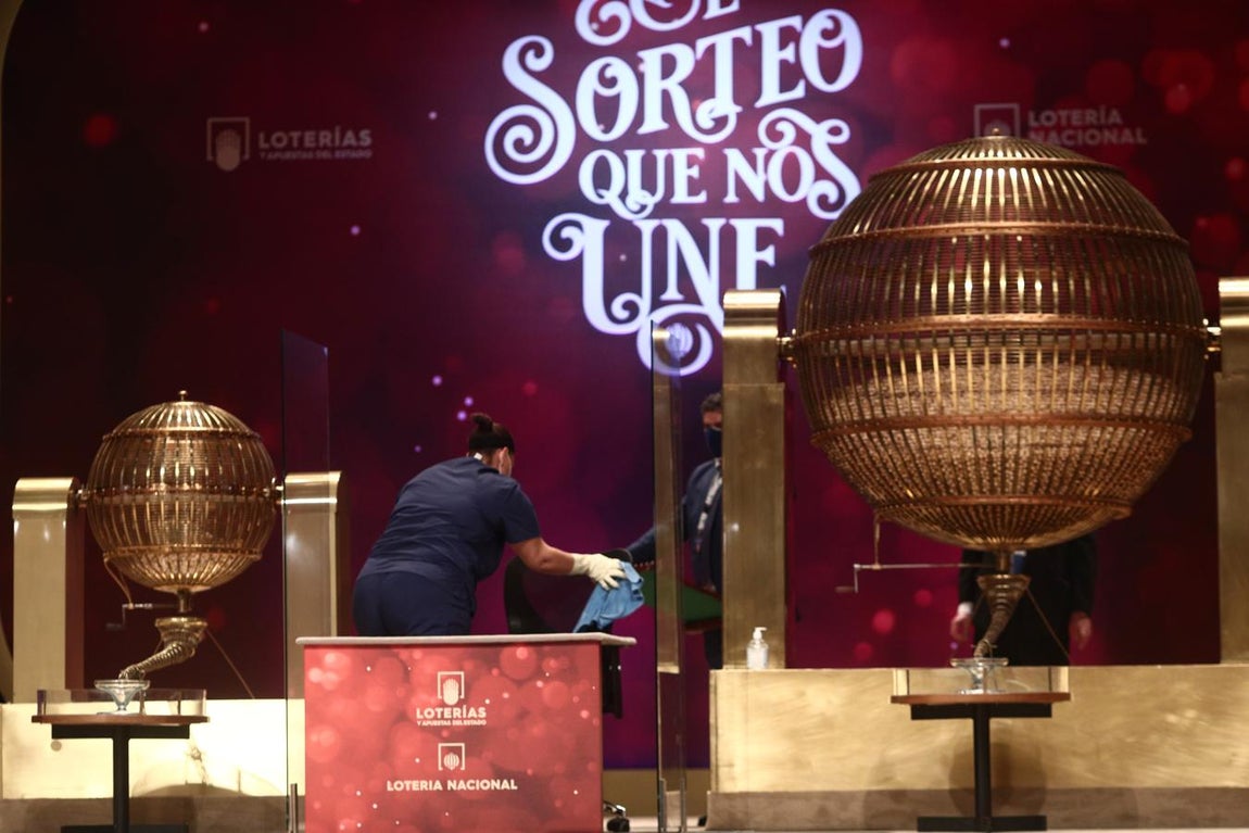 Una empleada limpia la mesa del sorteo para que se cumplan todas las medidas de higiene durante la celebración del Sorteo Extraordinario de la Lotería de Navidad 2020 en el Teatro Real.