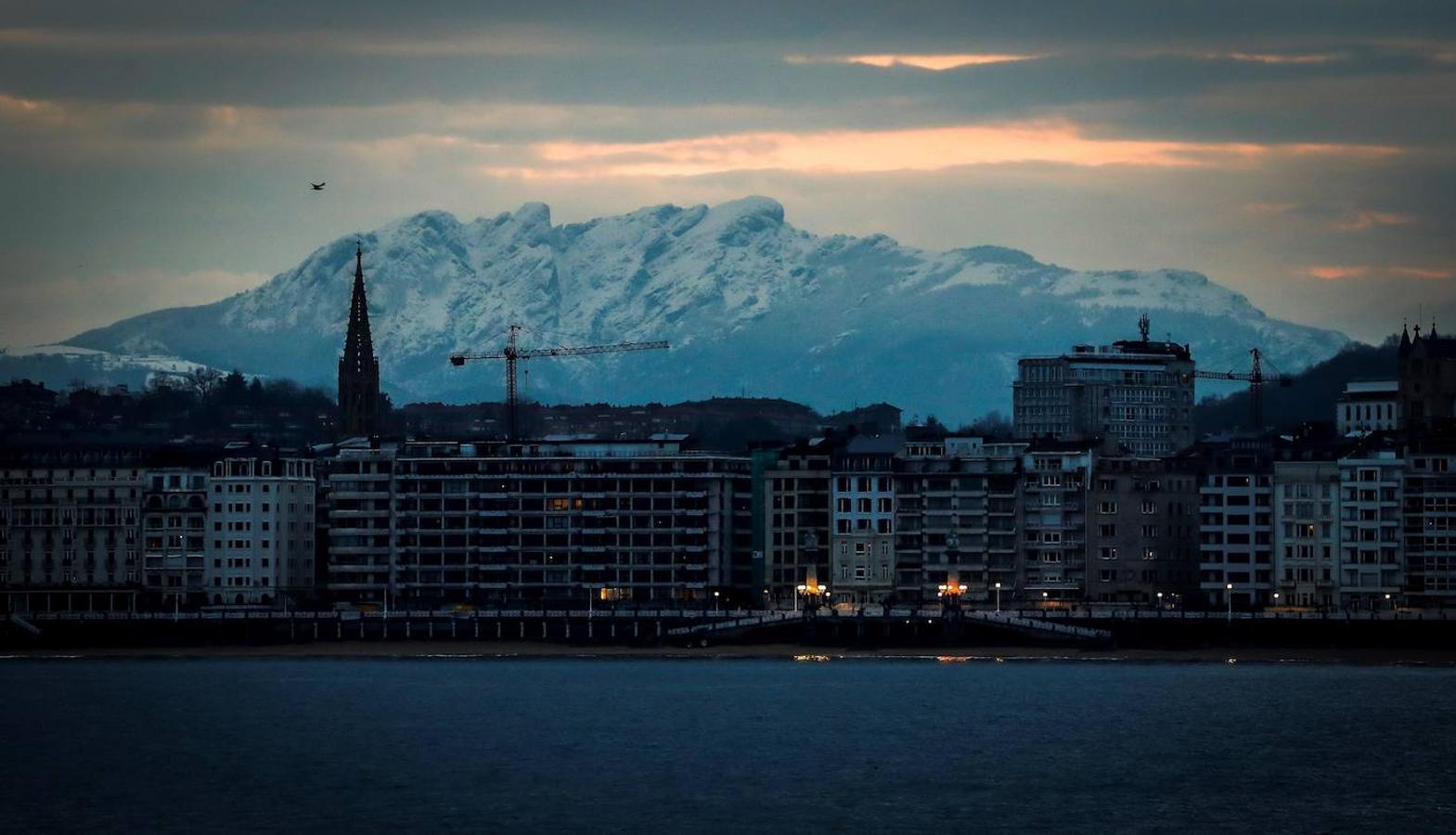 Vista de la Peñas de Aia nevadas junto a la playa de La Concha de San Sebastián, donde este martes los cielos amanecen muy nubosos y con precipitaciones en el País Vasco. 