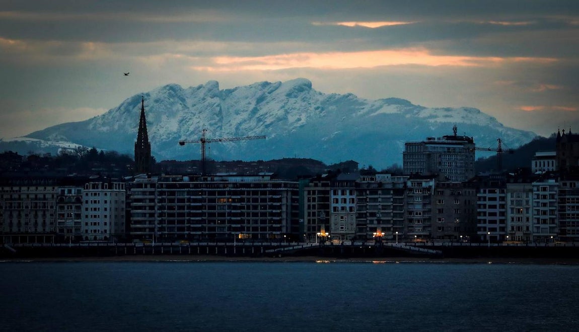 Vista de la Peñas de Aia nevadas junto a la playa de La Concha de San Sebastián, donde este martes los cielos amanecen muy nubosos y con precipitaciones en el País Vasco. 