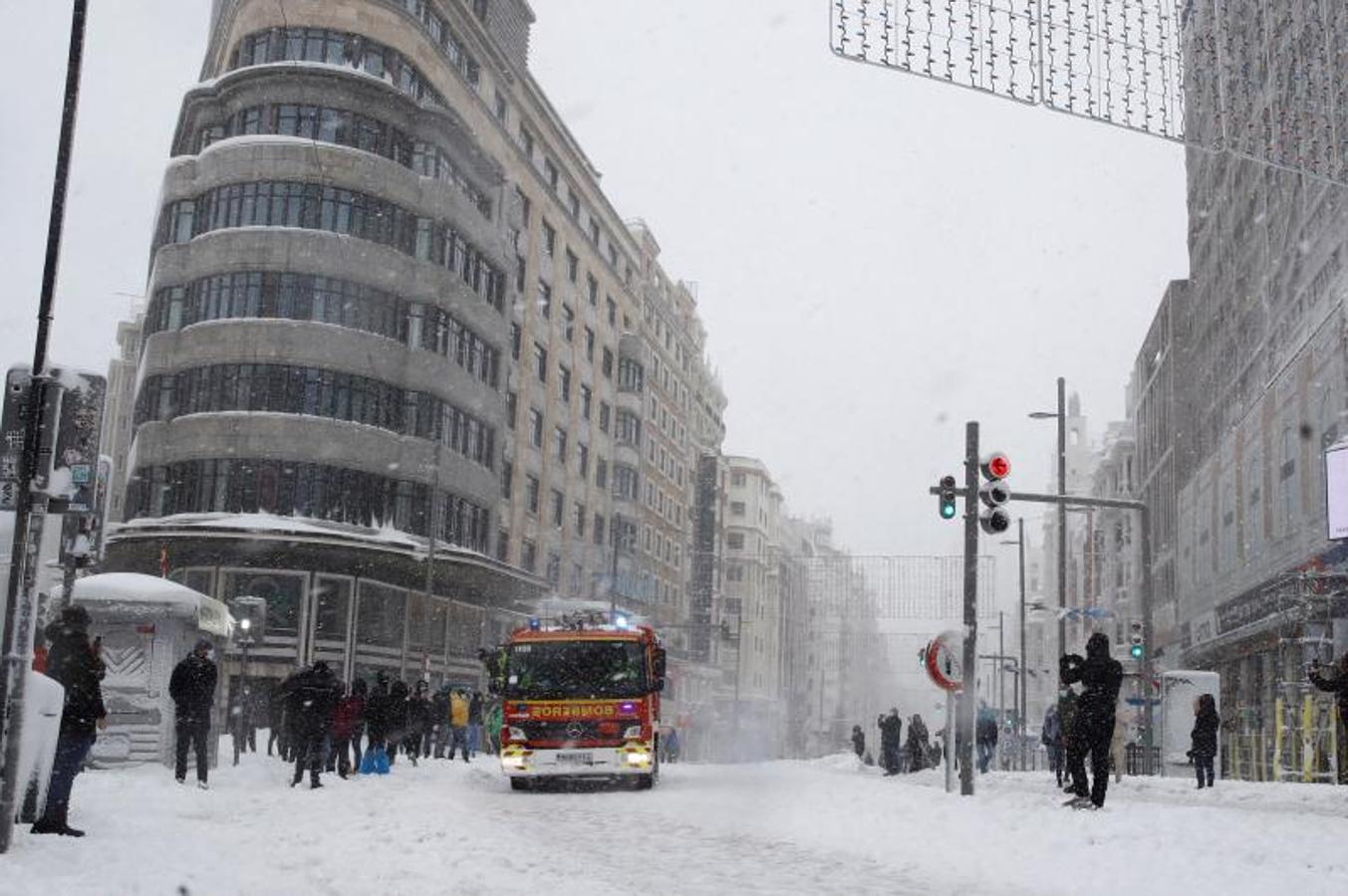 Bomberos en la Gran Vía. Varias personas pasean por la Gran Via cubierta de nieve en Madrid, mientras un camión de Bomberos trata de hacerse paso por el manto blanco que cubre esta arteria emblemática.