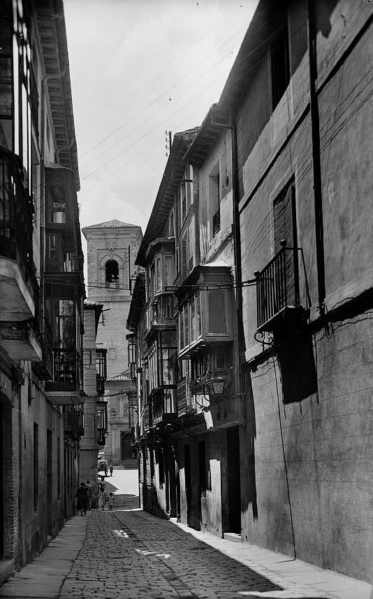 Calle de Alfonso X, al fondo el templo jesuita de San Ildefonso hacia 1952. Aquí los adoquines sustituyen al viejo suelo de guijarros, permaneciendo las antiguas aceras. Ediciones Artigot. Archivo Municipal de Toledo.. 