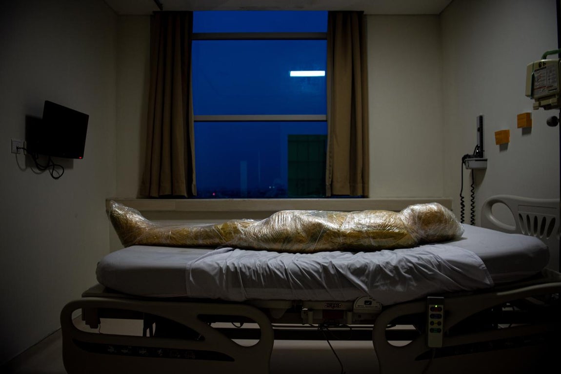 (Nominado al mejor fotografía de actualidad) El cuerpo de una presunta víctima del coronavirus yace, envuelto en plástico amarillo para desechos infecciosos, esperando una bolsa para cadáveres en un hospital de Indonesia.. 